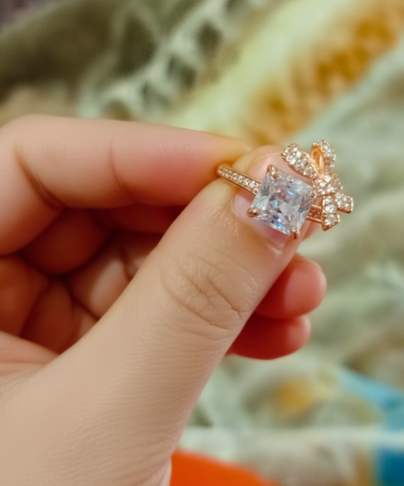 Rose gold ring with a large diamond held between fingers against a blurred background